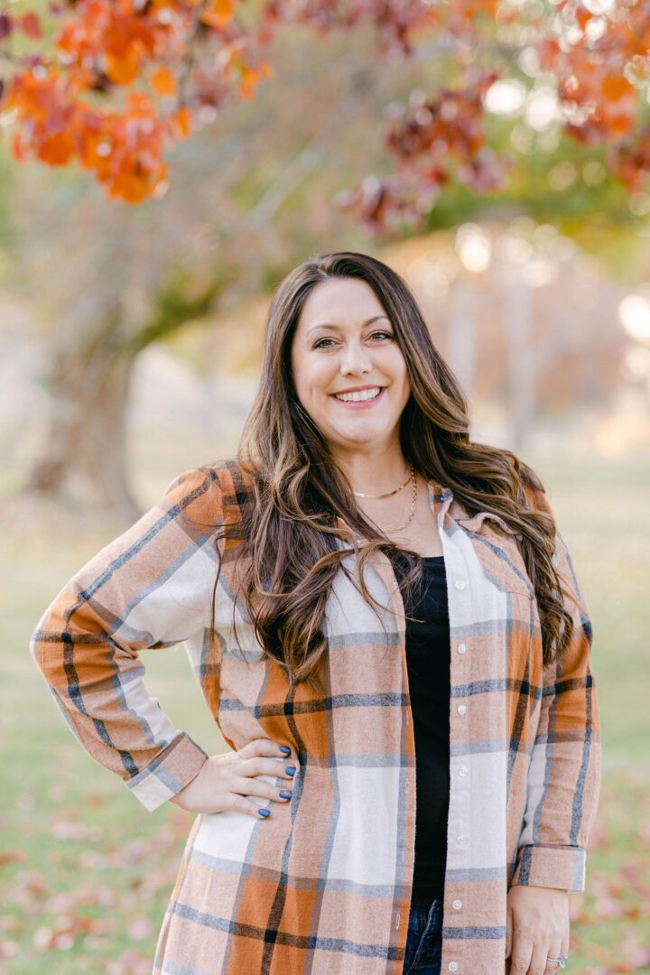 Smiling woman in plaid shirt outdoors with autumn colors.