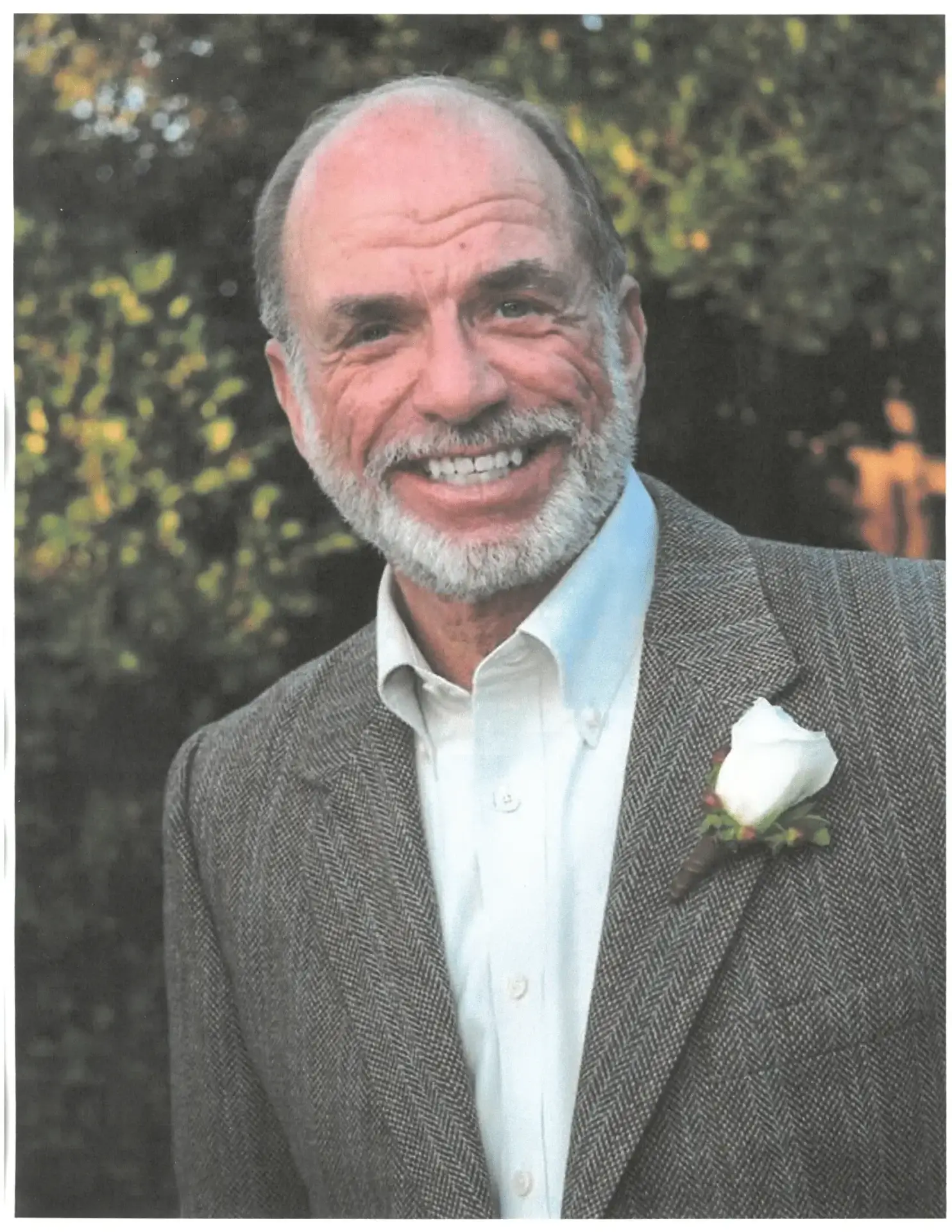 Smiling elderly man in a suit with a white rose boutonniere.