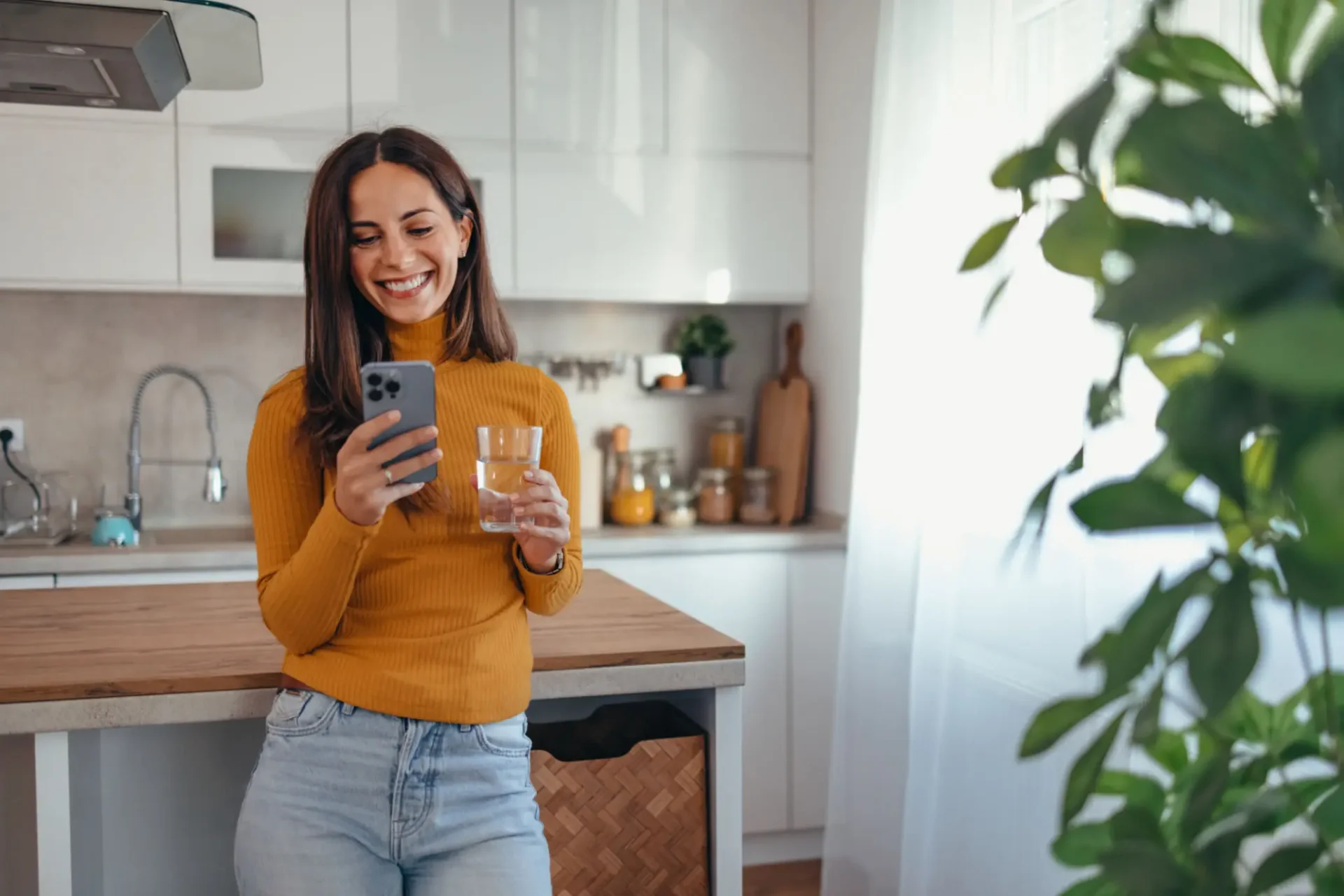 Woman enjoying a drink and a phone chat in a cozy kitchen.